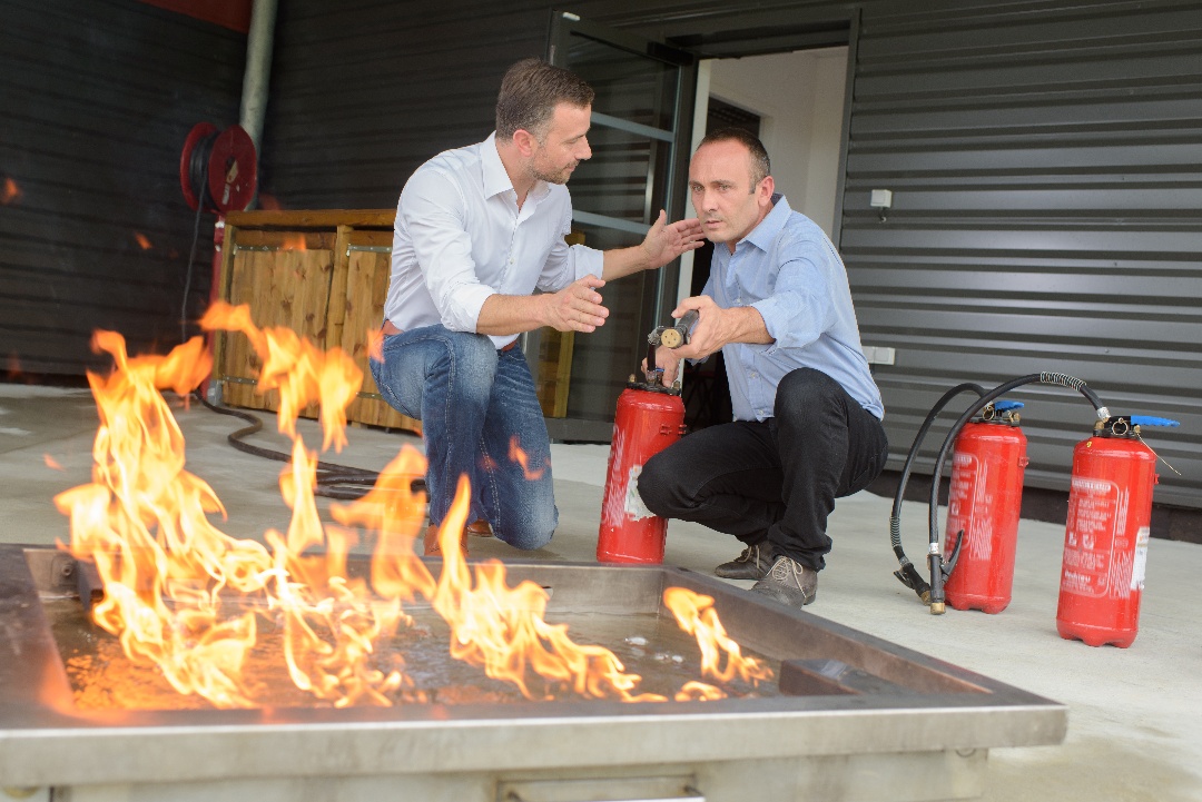 Two men testing fire extinguishers with flames 